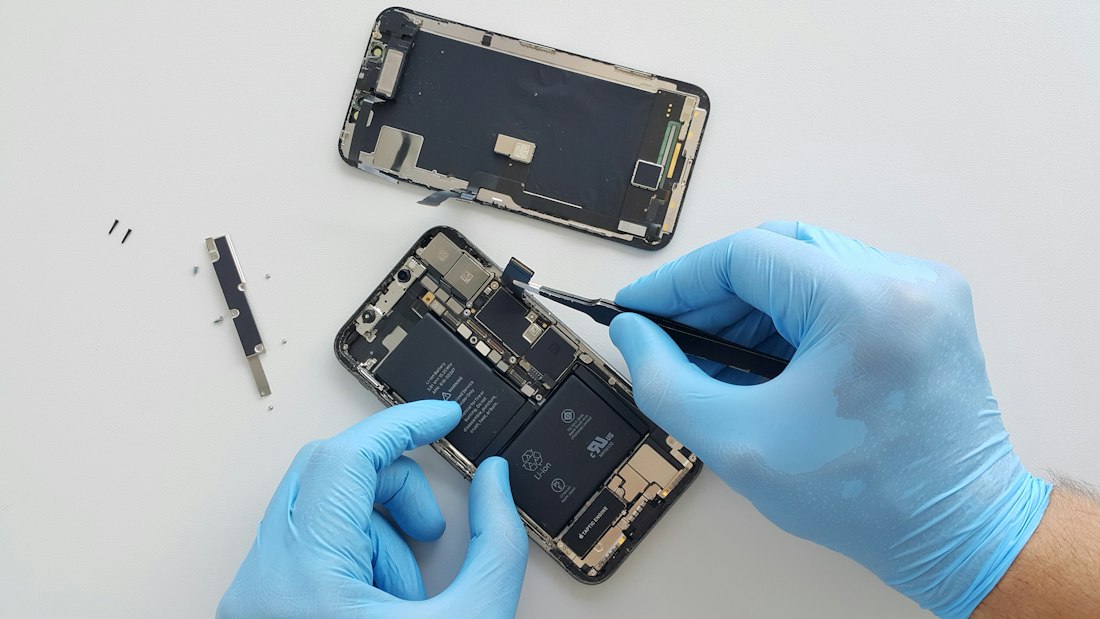 Composants internes d'un iPhone manipulés avec des gants d'atelier.
