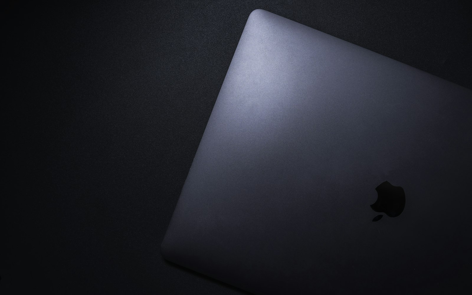 MacBook argenté fermé, posé sur un textile noir.